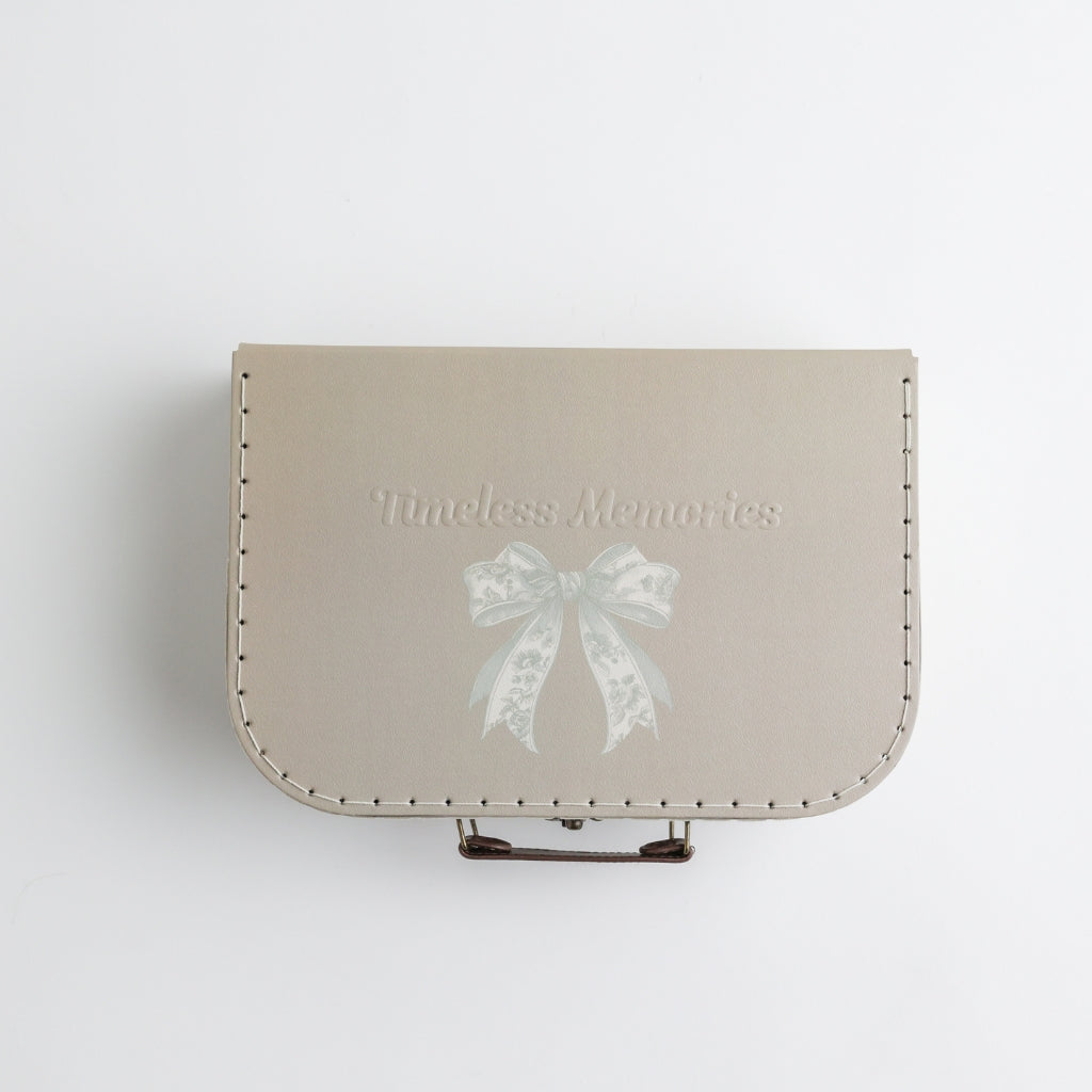 A beige keepsake suitcase with a subtle embossed bow illustration and "Timeless Memories" text for elegant baby keepsakes.