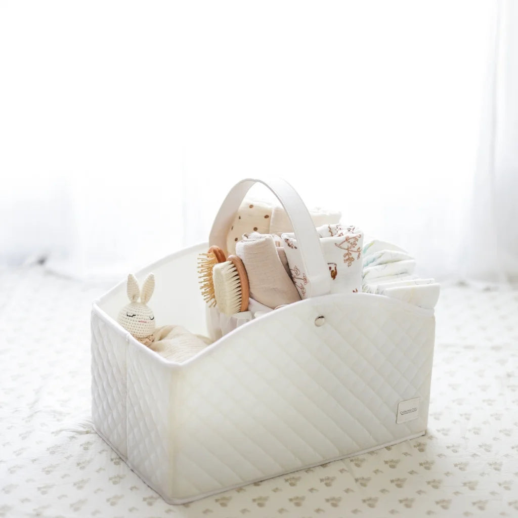 A white quilted baby storage caddy filled with baby essentials, set against a softly lit nursery background for a cozy aesthetic.
