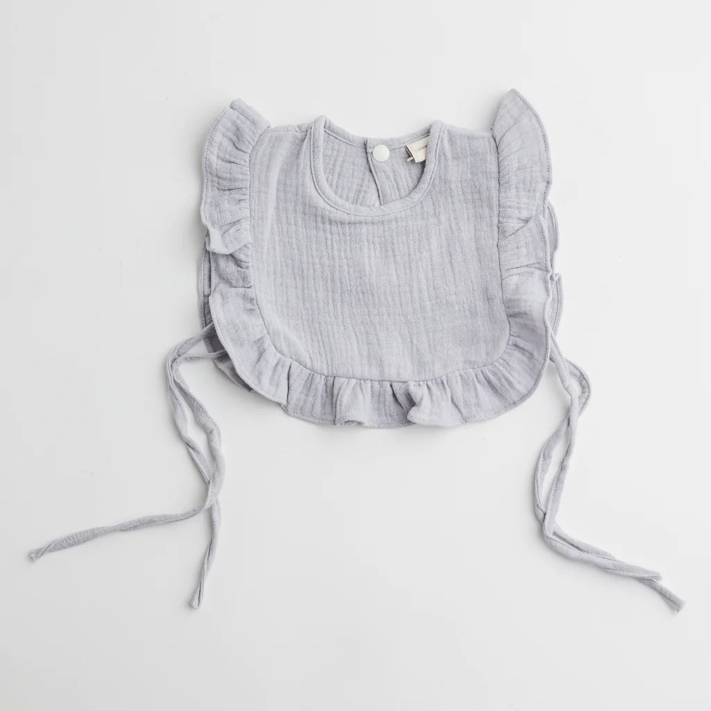 A close-up of a soft grey muslin ruffle bib featuring delicate frill details and adjustable ties for a secure fit.