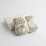 A soft sage baby blanket, presented with a matching luxury packaging box.