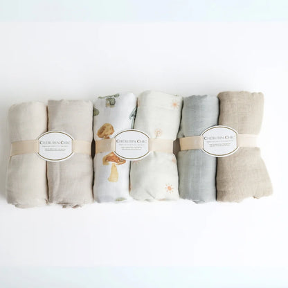 A neatly rolled set of Cherubin Chic muslin swaddle blankets in earthy tones and soft pastels, elegantly packaged for gifting or nursery use.