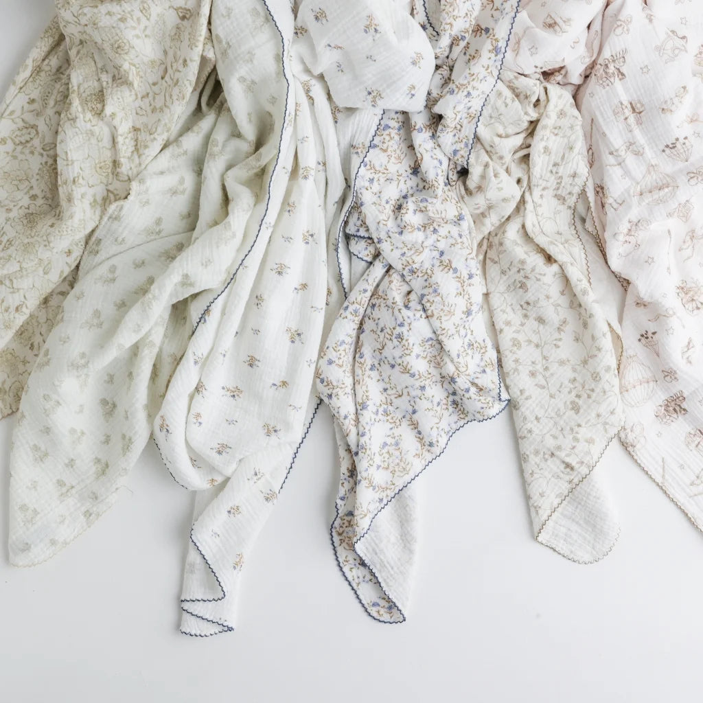 A stylish display of various baby swaddle blankets in floral, vintage, and neutral designs, draped elegantly.