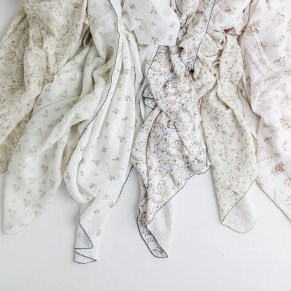 A stylish display of various baby swaddle blankets in floral, vintage, and neutral designs, draped elegantly.