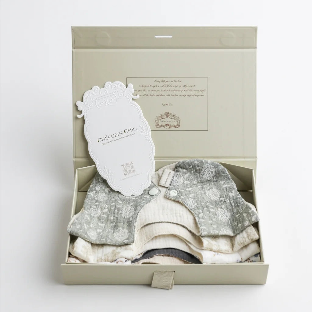 A beautifully packaged set of Cherubin Chic baby bibs in a premium keepsake box, featuring intricate detailing and a signature brand tag.