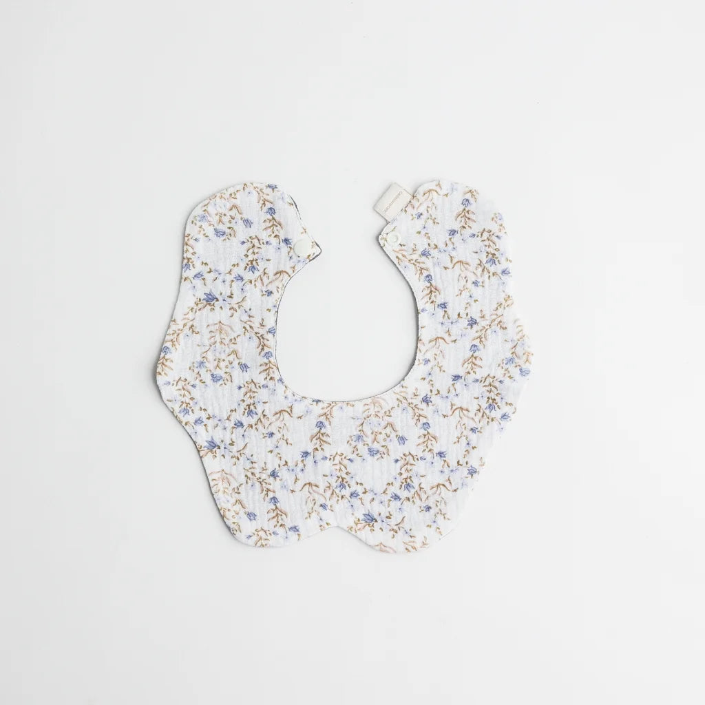 A charming baby bib adorned with a delicate blue and beige floral pattern, designed with premium organic cotton for comfort and style.