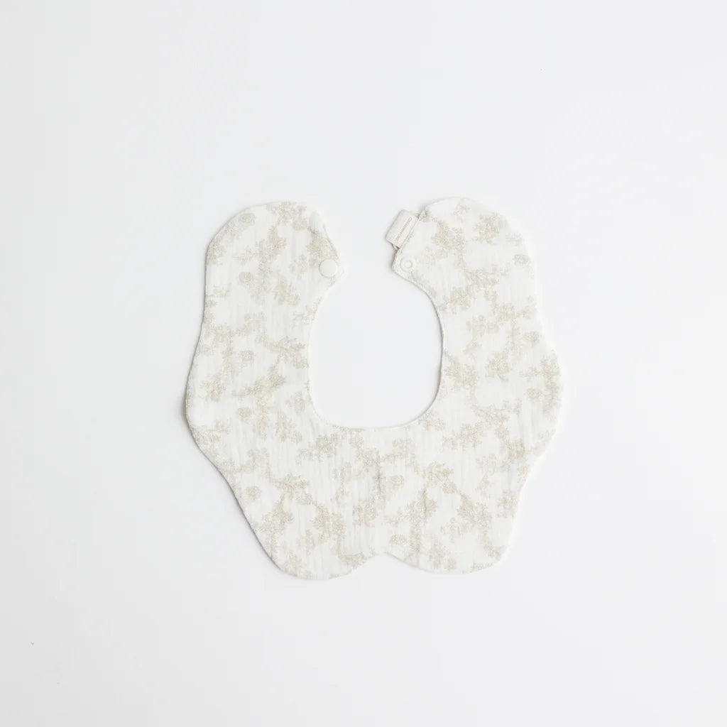 A soft white baby bib decorated with a subtle beige floral print, crafted for gentle wear on a baby’s delicate skin.