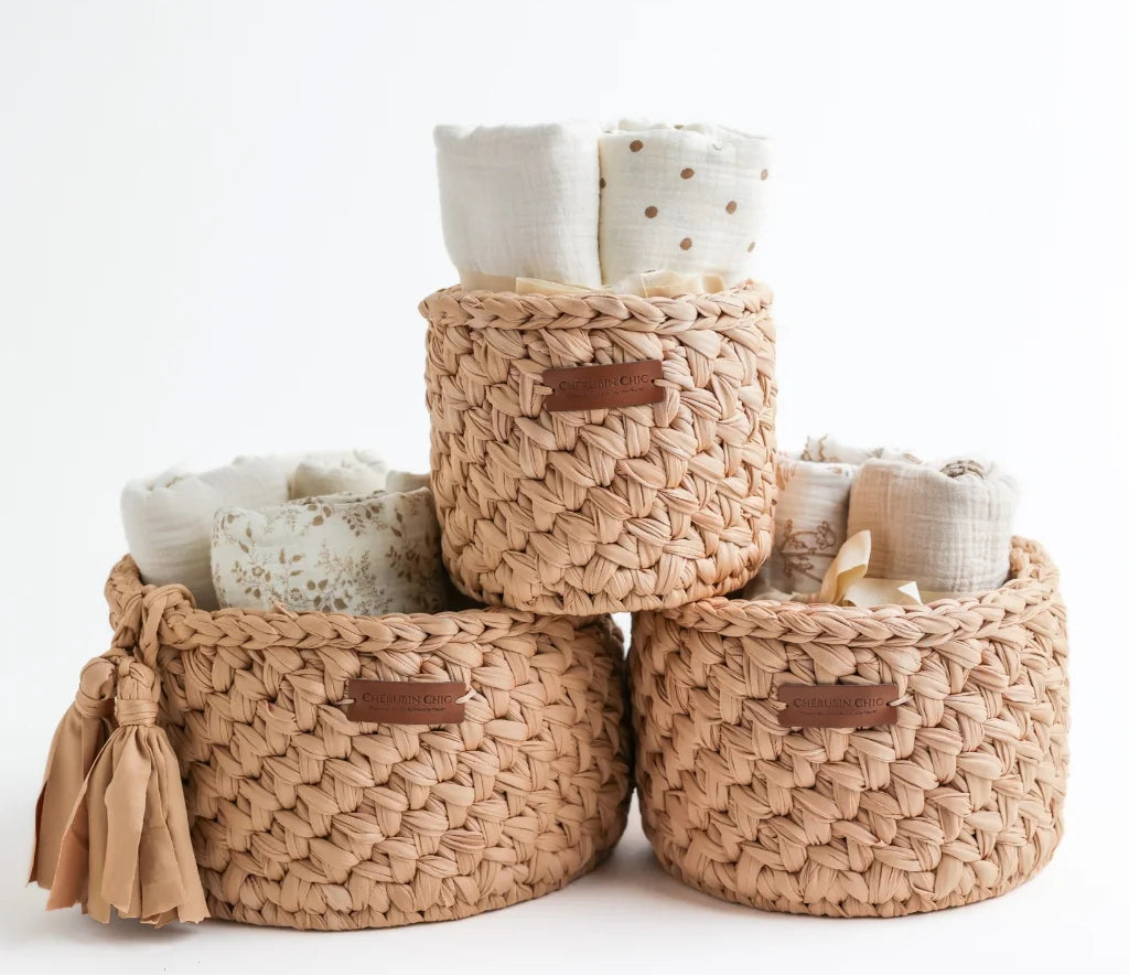 A set of three tan-colored Cherubin Chic storage baskets, each filled with soft, neutral-toned fabric items, making it an elegant nursery or home organization solution.