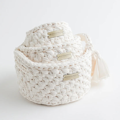 A trio of cream-colored woven knit storage baskets by Cherubin Chic, each adorned with a delicate brand label and a soft fabric tassel on the side.