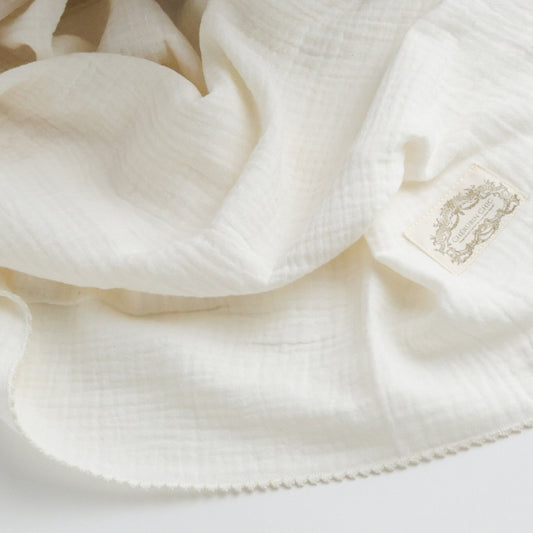 A soft and delicate ivory muslin swaddle blanket with a subtle textured weave, featuring a vintage Cherubin Chic label stitched to one corner.