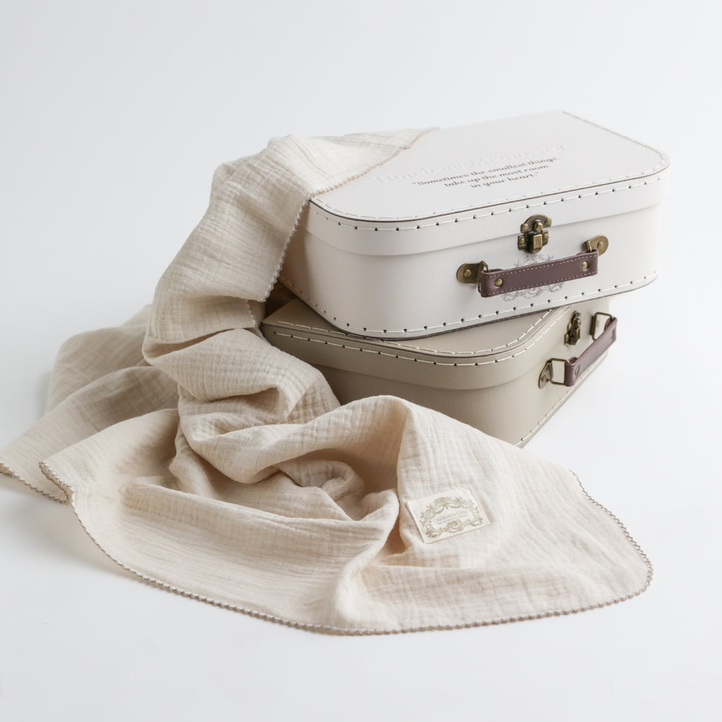 Two vintage-inspired memory suitcases displayed with a delicate beige baby blanket, showcasing a luxurious and timeless aesthetic.