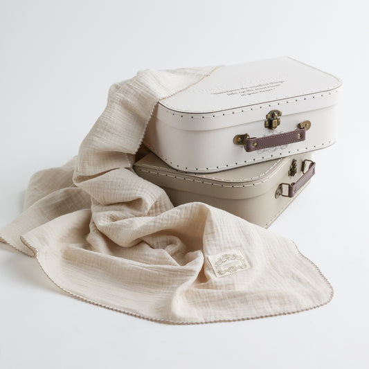 Two vintage-inspired memory suitcases displayed with a delicate beige baby blanket, showcasing a luxurious and timeless aesthetic.