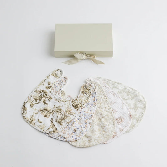 A set of five premium muslin baby bibs arranged neatly next to an elegant gift box. The bibs showcase different classic prints, including safari animals, floral, and vintage-inspired designs.