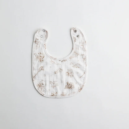 A soft muslin baby bib with a vintage-style print featuring delicate sketches of toys and animals on a white background. The bib has adjustable snap closures.