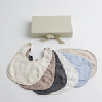 A set of six soft muslin baby bibs in neutral and pastel tones, displayed with an elegant gift box.