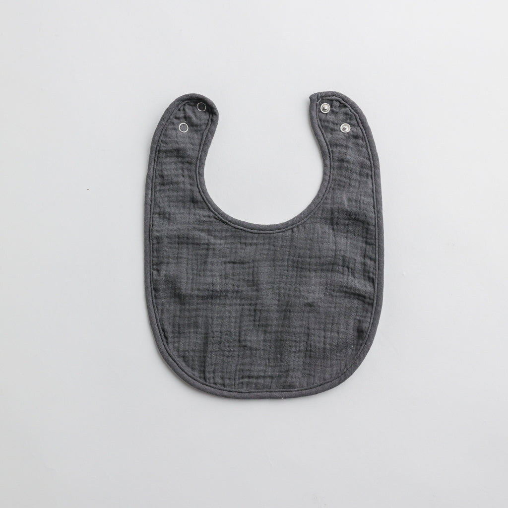 A dark gray muslin baby bib with adjustable snap buttons, designed for comfort and style.