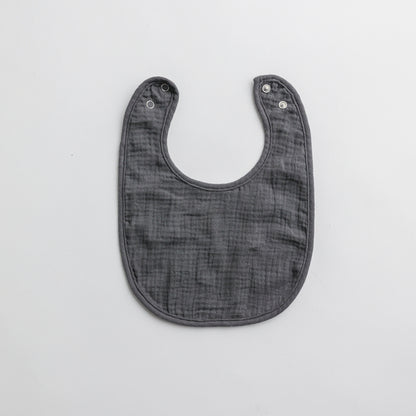 A dark gray muslin baby bib with adjustable snap buttons, designed for comfort and style.