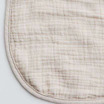 Close-up of a beige muslin baby bib, showcasing the soft and breathable fabric texture.