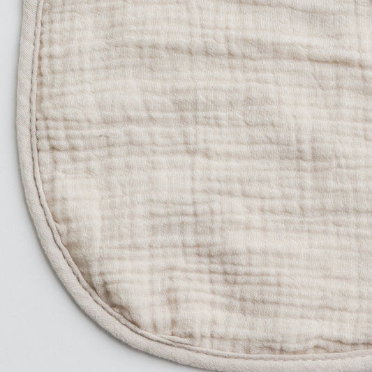 Close-up of a beige muslin baby bib, showcasing the soft and breathable fabric texture.
