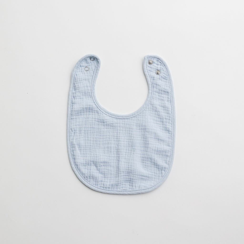 A light blue muslin baby bib with a minimalistic design and snap-button closure.