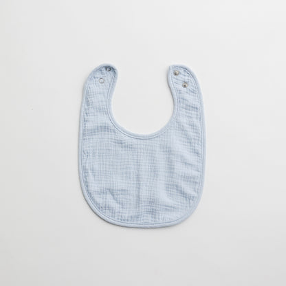A light blue muslin baby bib with a minimalistic design and snap-button closure.