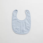 A light blue muslin baby bib with a minimalistic design and snap-button closure.