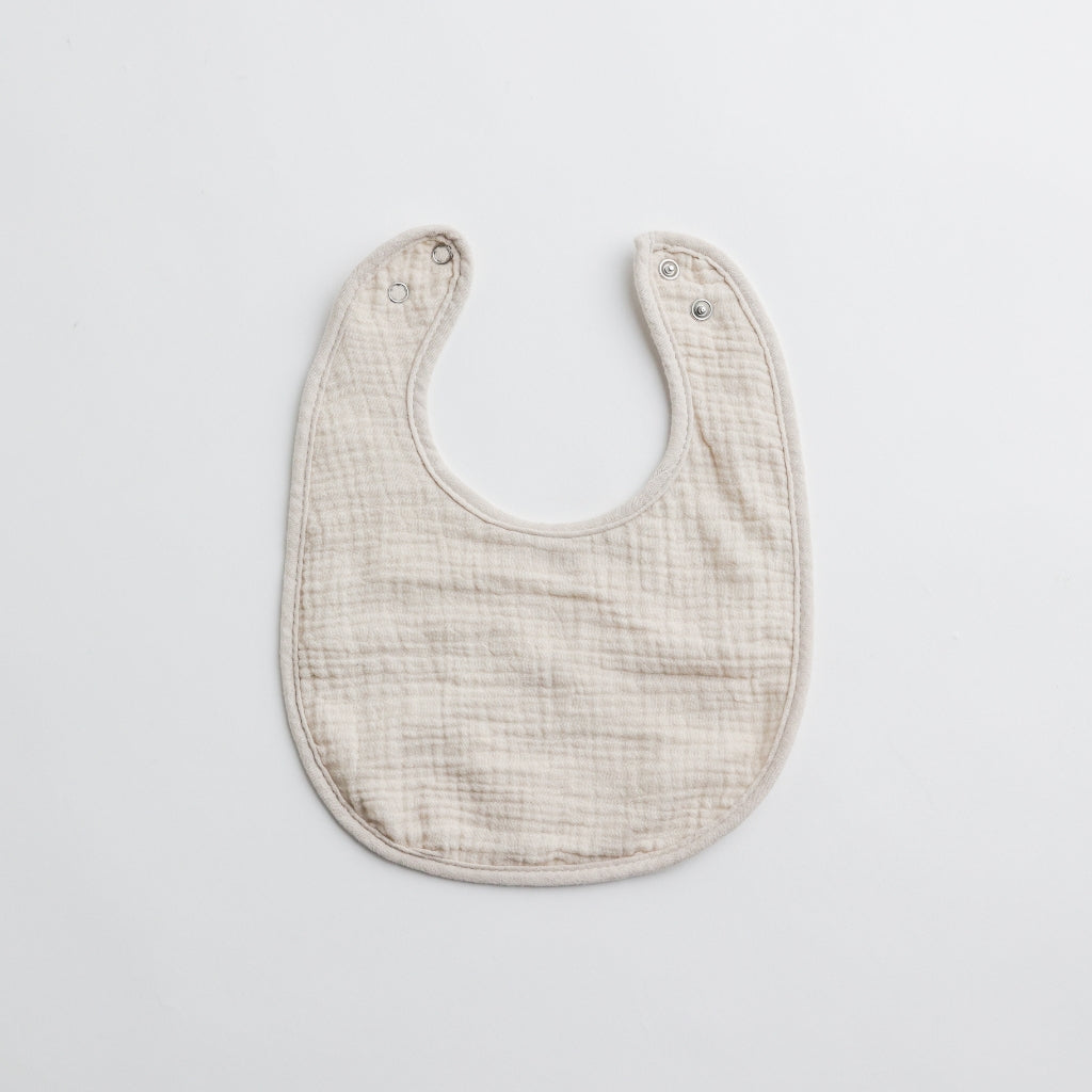 A neutral beige muslin baby bib, perfect for everyday use with a timeless aesthetic.