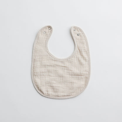 A neutral beige muslin baby bib, perfect for everyday use with a timeless aesthetic.