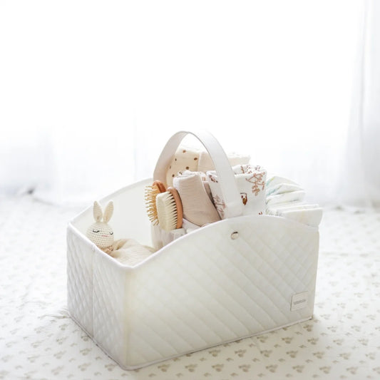 A white quilted baby storage caddy filled with baby essentials, set against a softly lit nursery background for a cozy aesthetic.