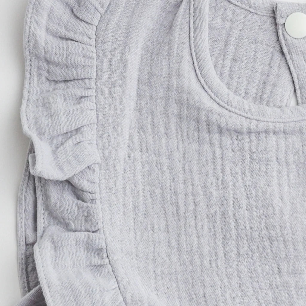 A close-up view of the ruffled edge and soft muslin fabric of a light gray bib, highlighting the intricate stitching.