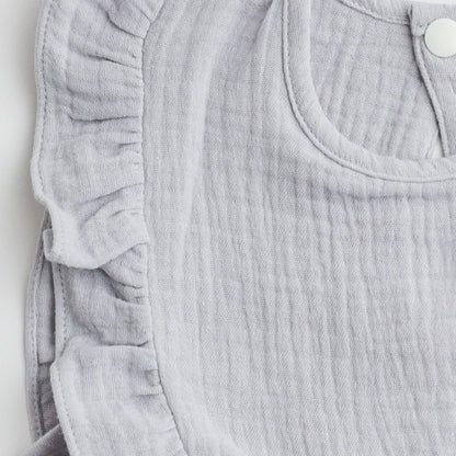 A close-up view of the ruffled edge and soft muslin fabric of a light gray bib, highlighting the intricate stitching.
