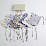 A beautifully arranged set of organic muslin ruffle bibs in various pastel and neutral tones, displayed alongside an elegant gift box.