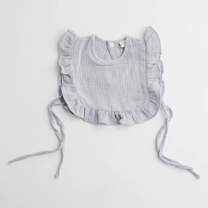 A close-up of a soft grey muslin ruffle bib featuring delicate frill details and adjustable ties for a secure fit.
