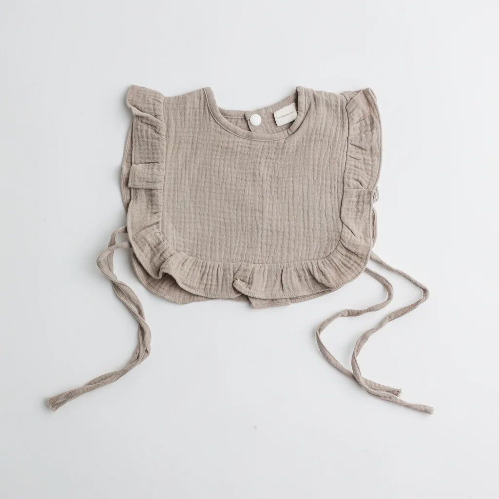 A taupe-colored muslin ruffle bib with frilly edges, showcasing a neutral and timeless design.