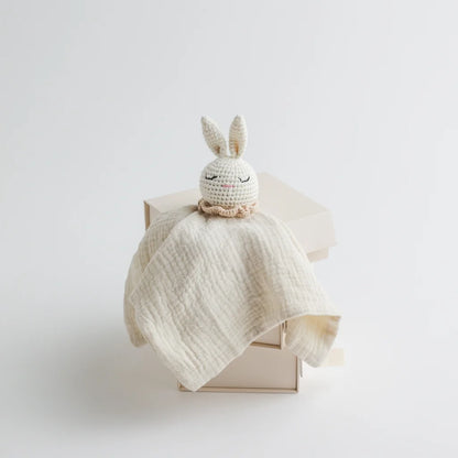 A soft cream muslin baby comforter with a sleepy-eyed crocheted bunny head, exuding a warm and comforting aesthetic.