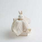 A soft cream muslin baby comforter with a sleepy-eyed crocheted bunny head, exuding a warm and comforting aesthetic.