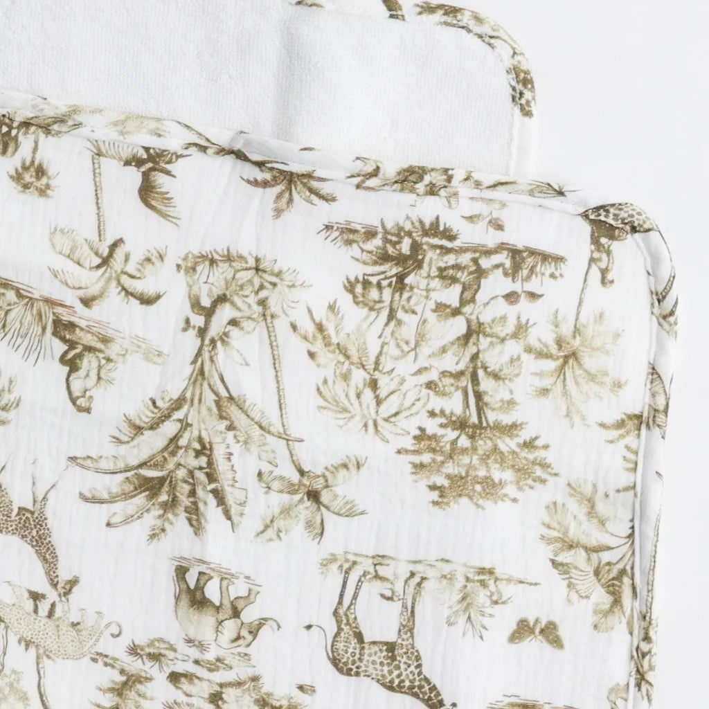 A close-up of a baby changing pad with a vintage safari animal print in muted earth tones, featuring giraffes, elephants, and palm trees.