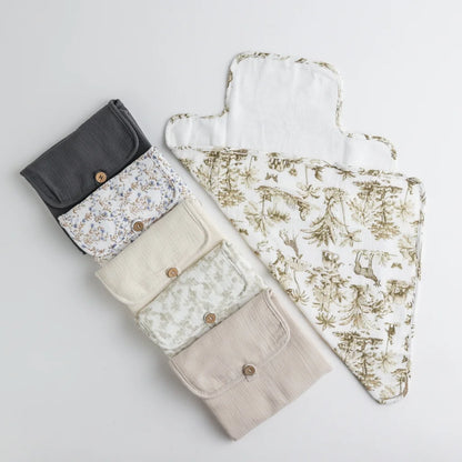 A set of six portable baby changing pads in various neutral and floral patterns, neatly folded with wooden button closures.