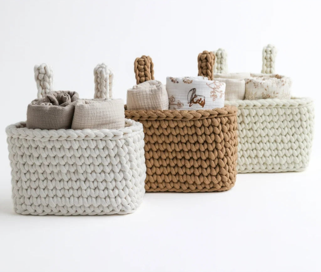 A set of three knit crib organizers in neutral tones—white, beige, and brown—neatly arranged and filled with swaddles, blending practicality with timeless aesthetics.