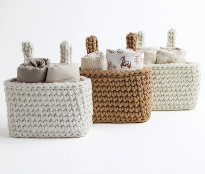 A set of three knit crib organizers in neutral tones—white, beige, and brown—neatly arranged and filled with swaddles, blending practicality with timeless aesthetics.
