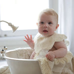 A baby wearing a vintage lace bib while sitting in a classic white bathtub, exuding a soft and elegant aesthetic.