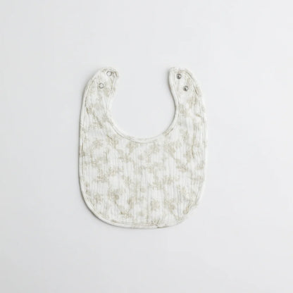 A vintage-inspired muslin baby bib in soft beige with delicate floral patterns, featuring a snap closure for easy use.