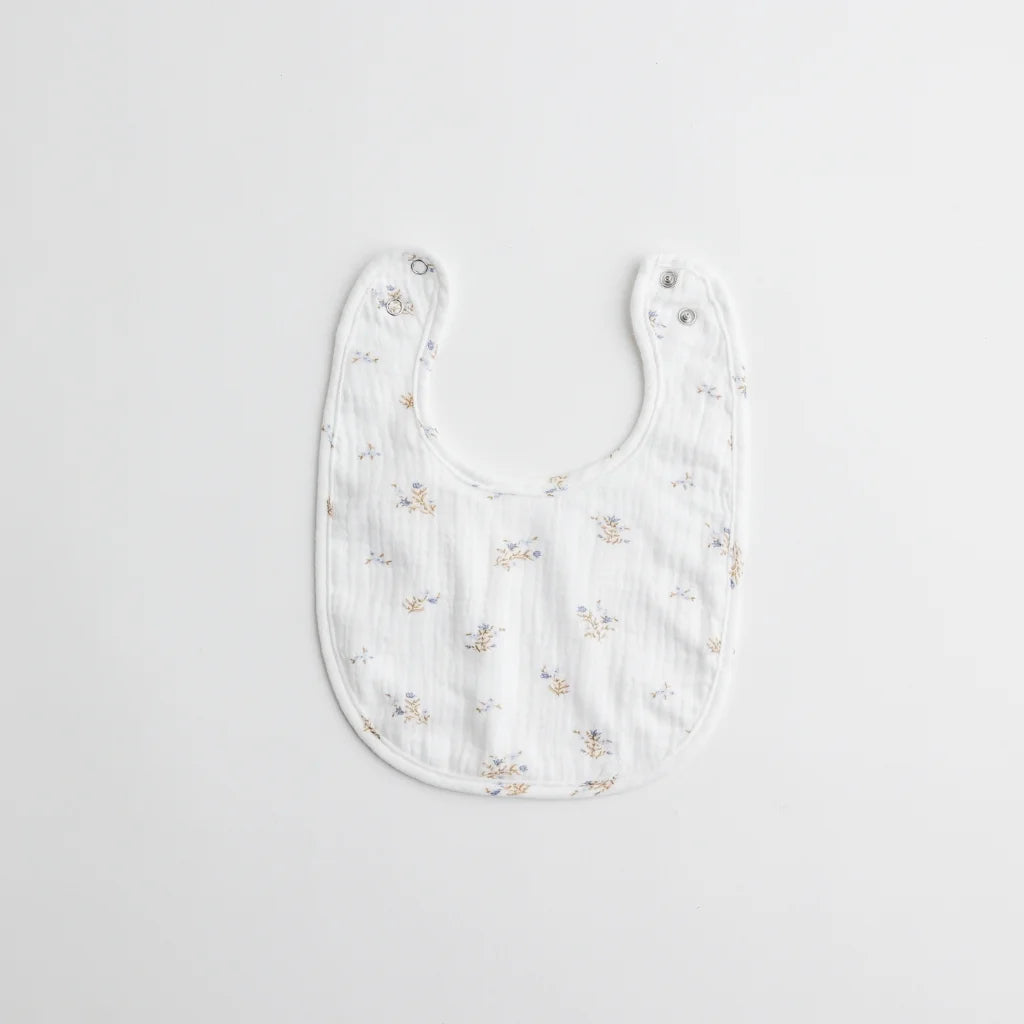 A white muslin baby bib with small blue floral prints, designed with dual snap closures for adjustable fit.