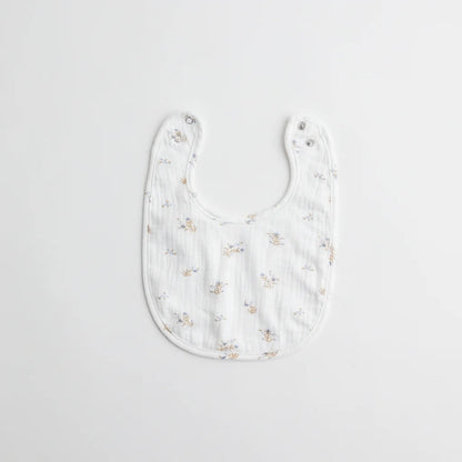 A white muslin baby bib with small blue floral prints, designed with dual snap closures for adjustable fit.