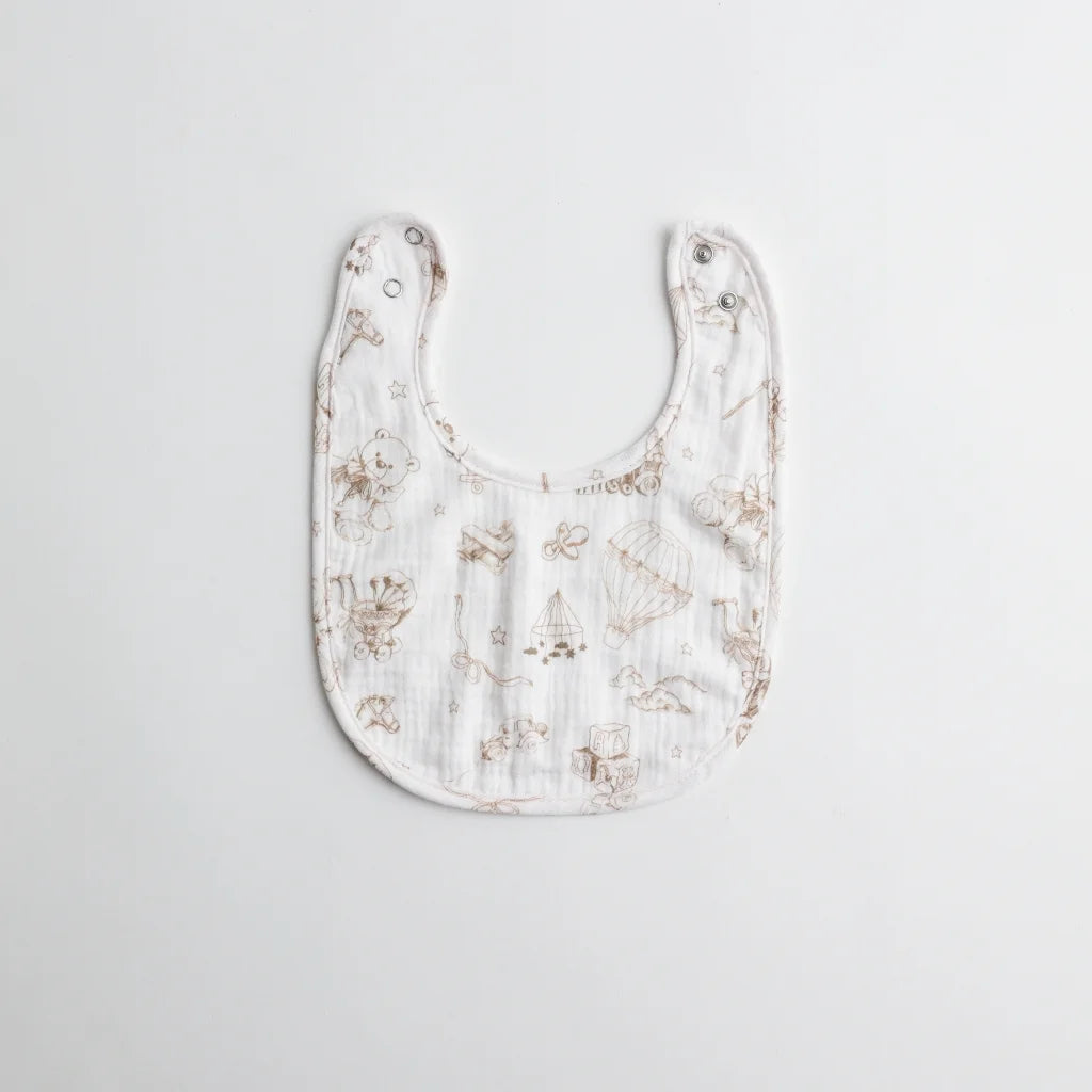 A classic muslin baby bib with a hand-drawn teddy bear and toy pattern in neutral brown tones.