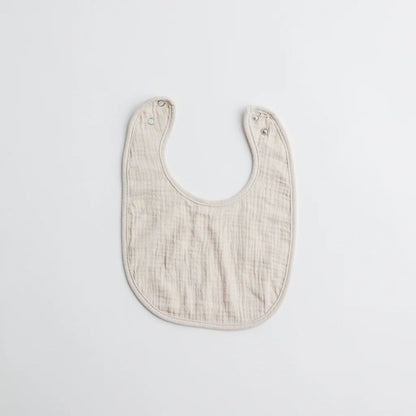 A plain beige muslin baby bib with a soft texture and snap buttons for secure fastening.